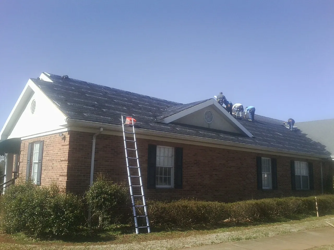 Crew tearing shingles off a brick ranch roof with a ladder set — Metal Roof Repair work by our crew in Strasburg