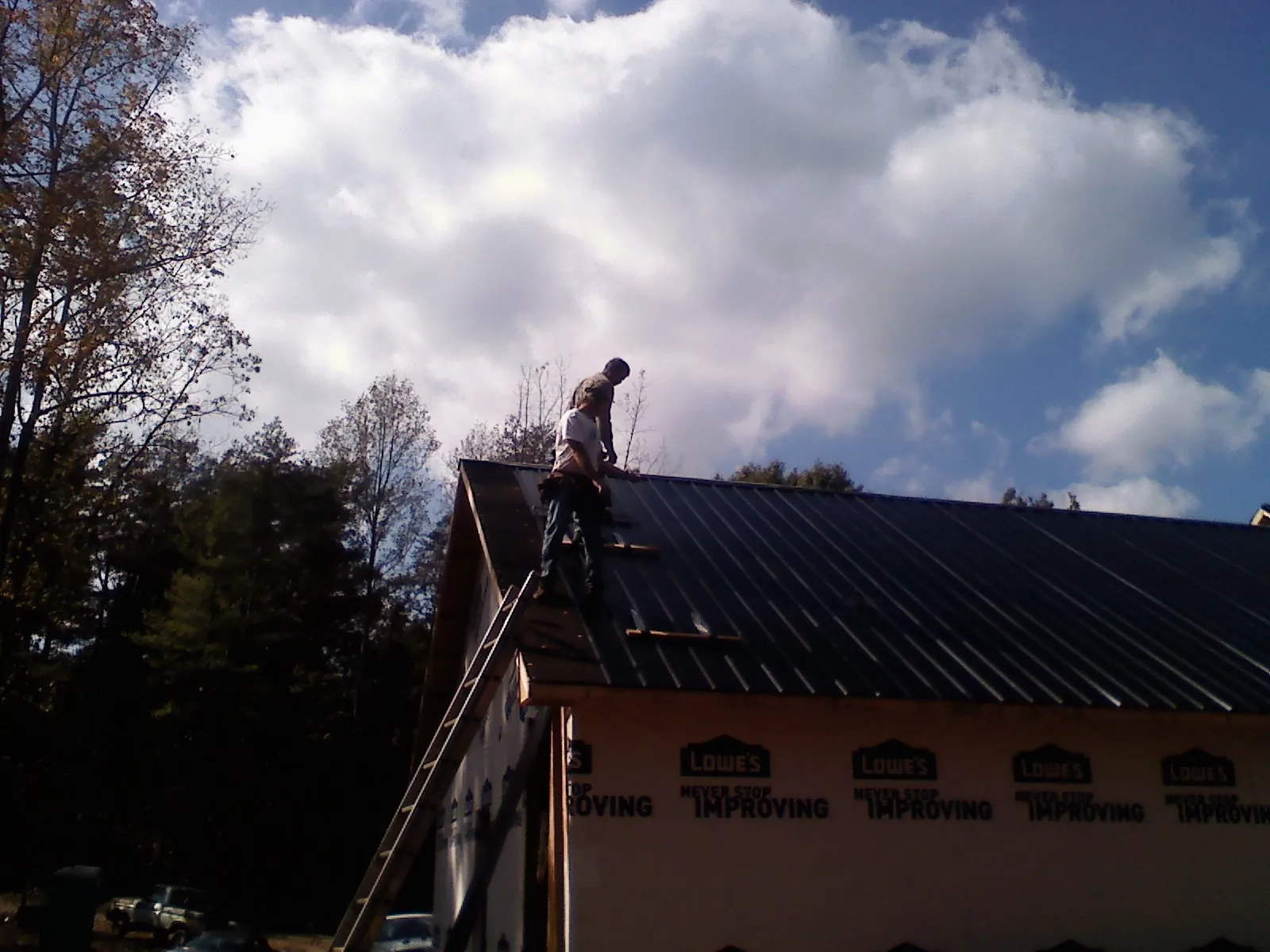 Roofer fastening dark metal panels high against a cloudy sky, from a Roof Inspection job in Strasburg